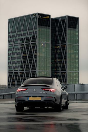 A vertical of a matte grey Mercedes AMG car parked in front of modern building for a photoshoot