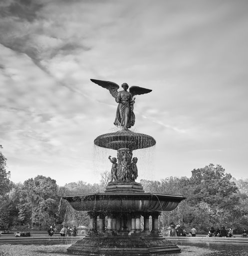 A greyscale of the Bethesda Terrace and the fountain in a park surrounded by trees under a cloudy sky