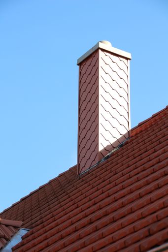 A low angle shot of a tiled roof with a new chimney against a blue sky