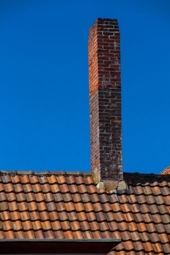 A vertical shot of a tiled roof with a new chimney against a blue sky