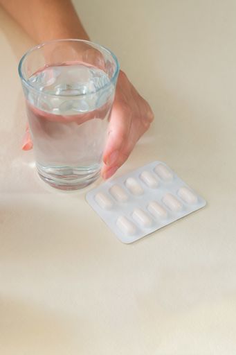 A vertical shot of a woman's hands with a glass of water and a tablet pills blister