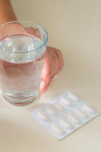 A vertical shot of a woman's hands with a glass of water and a tablet pills blister