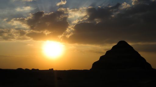 View of the shape the Pyramid of Djoser or Step Pyramid at the necropolis of Saqqara, near Cairo (Egypt) at sunset with dark clouds. Backlight pho