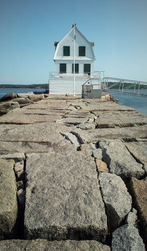 A vertical shot of a white wooden cottage on the rocky pier by the ocean