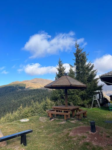 A vertical shot of a wooden table with benches on a hill against green mountains