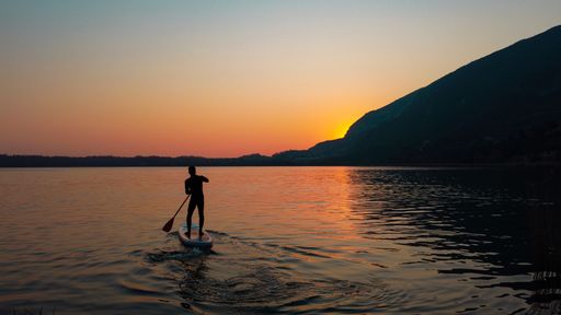 A silhouette of a man on a stand-up paddle board in Lake Como with a golden sunset in the background