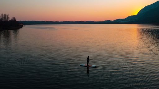 A silhouette of a man on a stand-up paddle board in Lake Como with a golden sunset in the background