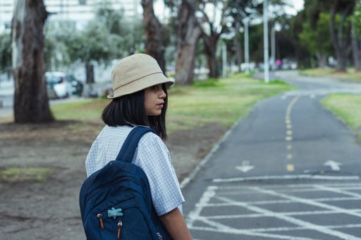 A Caucasian woman wearing a hat and a backpack and walking in the park