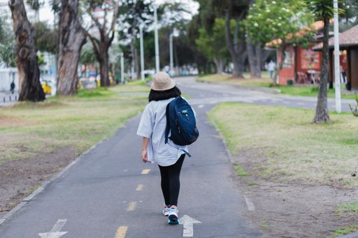 A Caucasian woman wearing a hat and a backpack and walking in the park