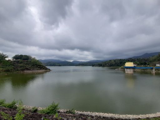 Water reservoir lake with reflections from cloudy sky with small bridge to a building and a dam at Bendungan Sermo, Kulonprogo, Java, Indonesia
