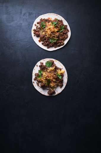 A vertical high angle shot of two tortilla bread with meat and melting cheese on a black surface