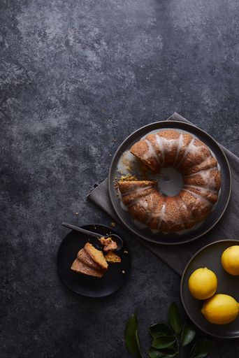 A vertical shot of lemon cake covered with sweet sauce near a plate of lemons on a black surface