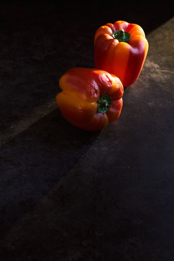 A vertical shot of two red peppers on a black surface