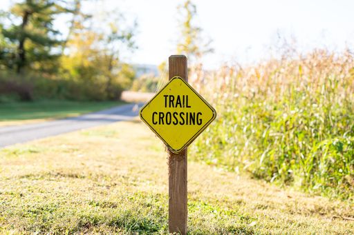 A closeup photo of a trail crossing sign with a rural scene blurred in the background