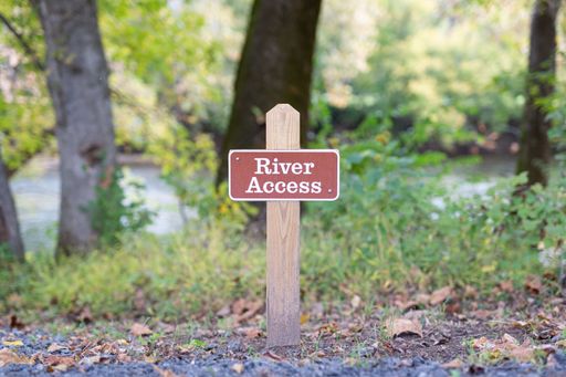 A closeup shot of red River Access Sign on the street with trees in the background