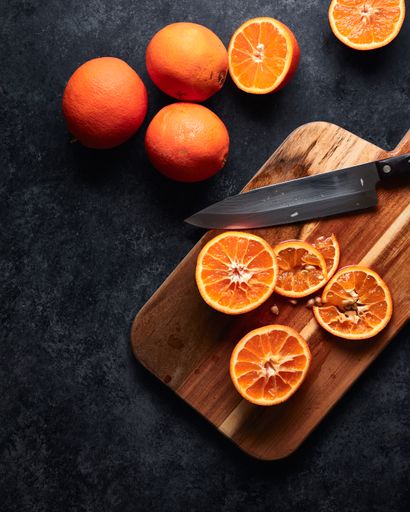 A vertical shot of sliced oranges and a knife on a chopping board on a black background