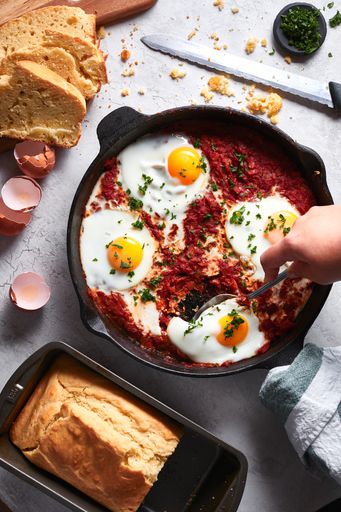 A vertical high angle shot of a person eating fried eggs with tomato sauce near slices of bread on a white table