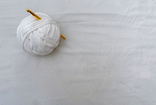 A top view closeup of a white t-shirt yarn ball with gold crochet hook isolated on white background