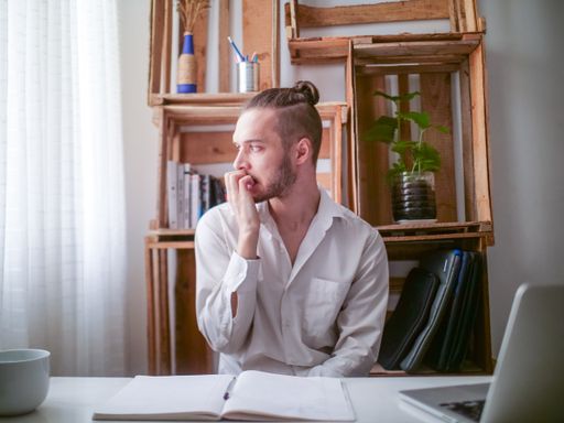 Young Caucasian Man in White Shirt Sitting at a Desk is Nervously Biting his Nails