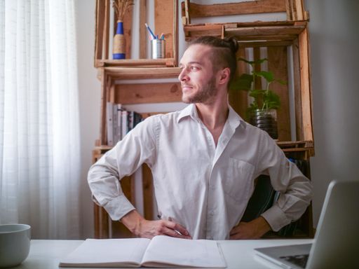 Young Caucasian Man in White Shirt Sitting at a Desk Stares at the Window Looking Proud and Satisfied