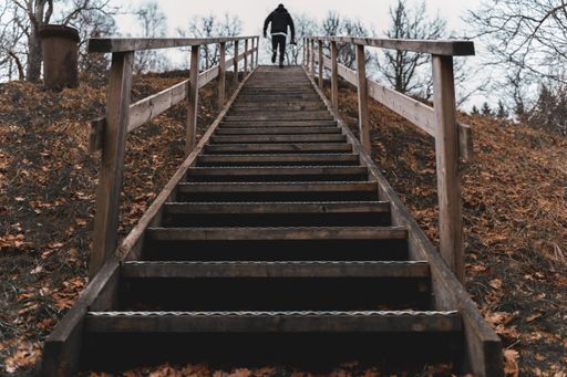 A low angle shot of a person going up the wooden stairs surrounded by a lot of fallen autumn leaves