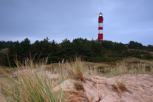 The Leuchtturm Amrum lighthouse on a hill covered in the grass under a cloudy sky in the evening in Nebel, Germany