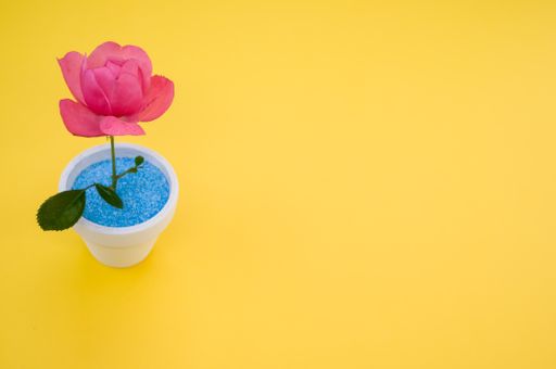 A closeup of a decorative artificial pink rose in a pot on the yellow surface - space for text