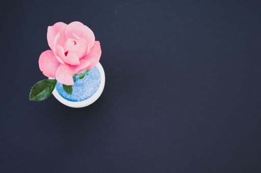 A top view of a decorative artificial pink rose in a pot on the black surface - space for text