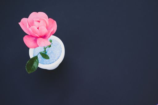 A top view of a decorative artificial pink rose in a pot on the black surface - space for text
