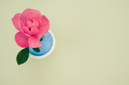 A top view of a decorative artificial pink rose in a pot on the green surface - space for text