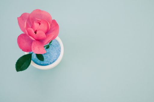 A top view of a decorative artificial pink rose in a pot on the green surface - space for text