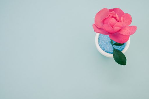 A top view of a decorative artificial pink rose in a pot on the green surface - space for text