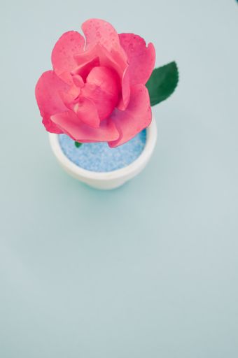 A top view of a decorative artificial pink rose in a pot on the green surface - space for text