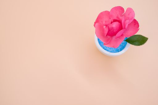 A top view of a decorative artificial pink rose in a pot on the orange surface - space for text