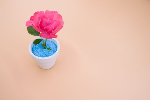 A closeup of a decorative artificial pink rose in a pot on the orange surface - space for text