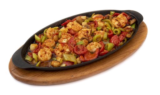 A closeup of a dish with shrimps served on a black plate on a wood board isolated on a white background