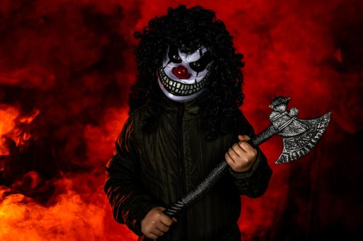 A scary Halloween clown holding an axe with smoke fire in the background