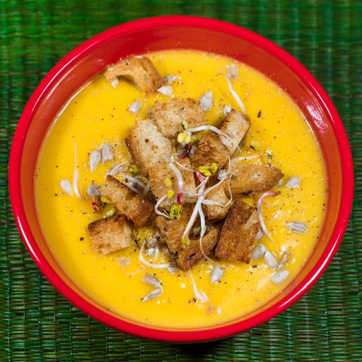 A high angle shot of a yellow soup with meat and onions on a green surface