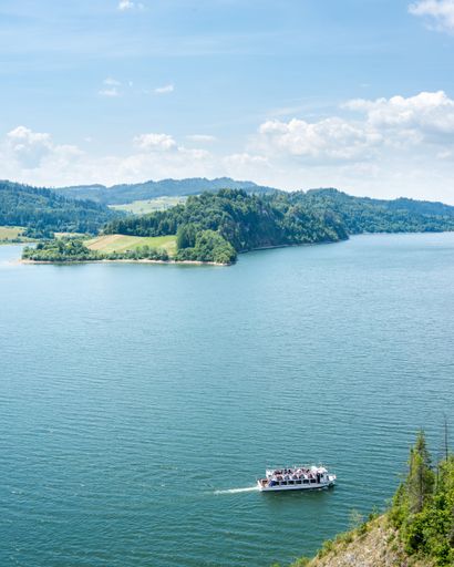 A vertical high angle shot of a white ship in the lake surrounded by high mountains