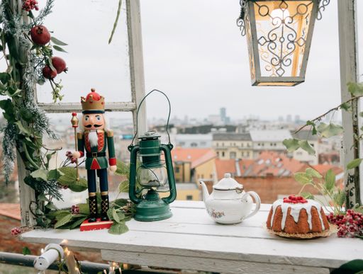A nutcracker ornament, a cake, and a lantern on a wooden table facing the city