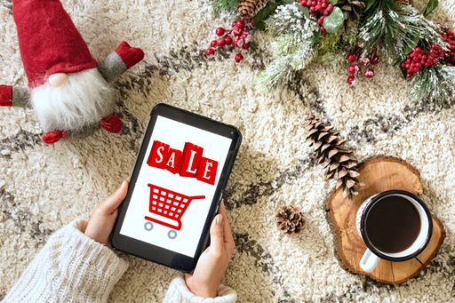 A top view of a caucasian woman holding a tablet showing a Christmas sale, next to decorations and a cup of coffee