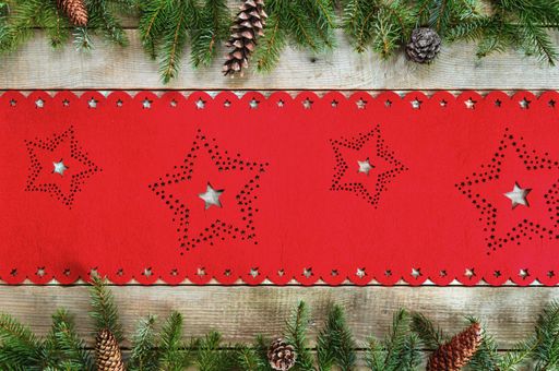 A top view of a wooden surface with a red Christmas table cloth, fir leaves, and cones on it