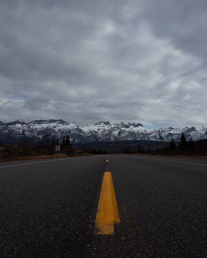A vertical shot of a road that leads to the snow-covered mountains on a cloudy day