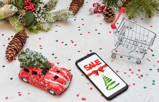 A closeup of a smartphone showing Christmas sale, on a surface filled with toys, pine cones and leaves, present, and a small shopping cart