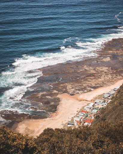 A high angle shot of the ocean and beach houses as seen from a grassy cliff in the coast of New South Wales, Australia
