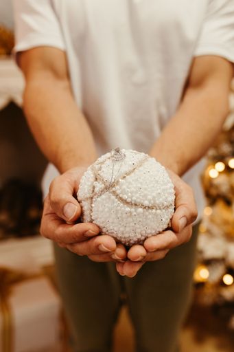 A vertical shot of a male holding a white ball decorated with pearls and a necklace