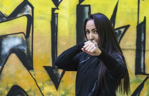 A girl in a black suit stands in a boxing stance against the background of the wall and looks into the camera. Focus on the girl's eyes.