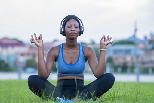 A shallow focus shot of an African female meditating while witting on the grass in a park