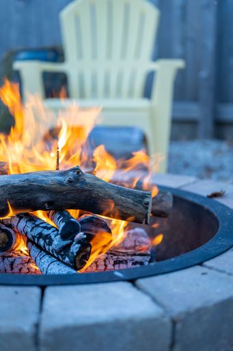 A vertical shot of a stone fire pit on a fall day with a white garden chair in the blur background