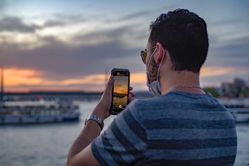 A shallow focus shot of a Hispanic male recording the sunset on his mobile phone